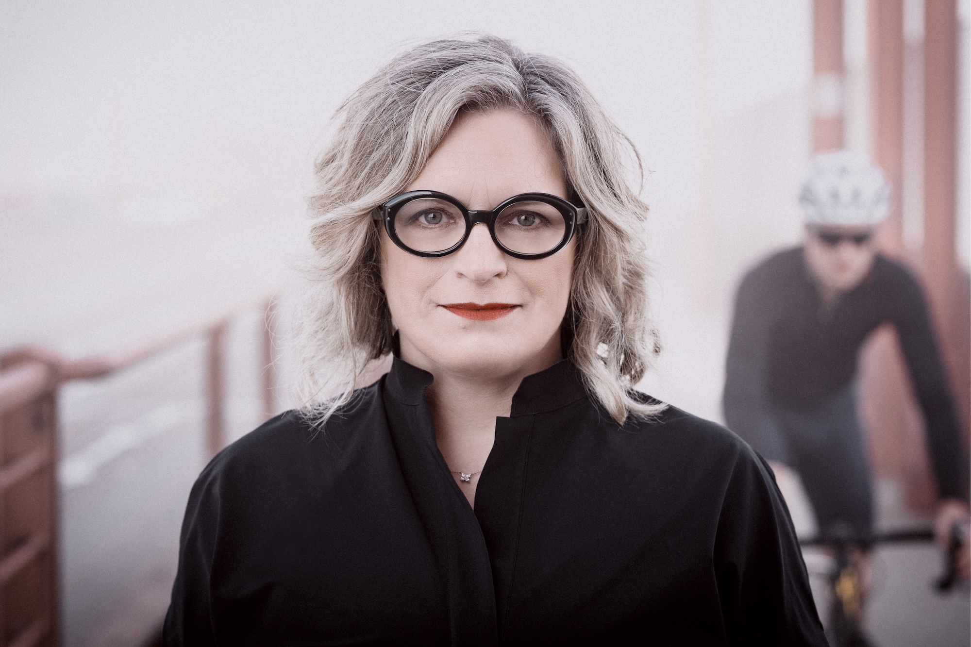 Janice on the golden gate bridge in business attire. A bicycle is fast approaching from behind.